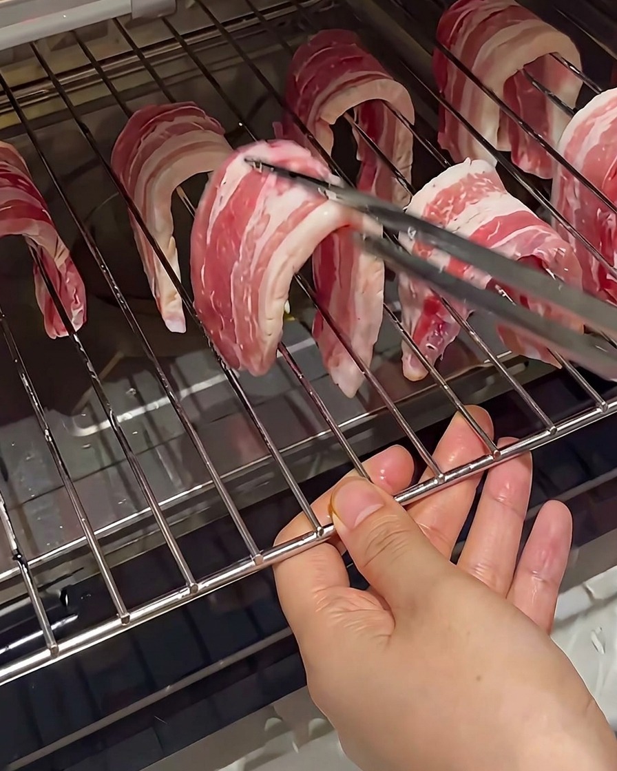 トングを使って、オーブンラックの網に豚バラ肉を吊るしている様子。