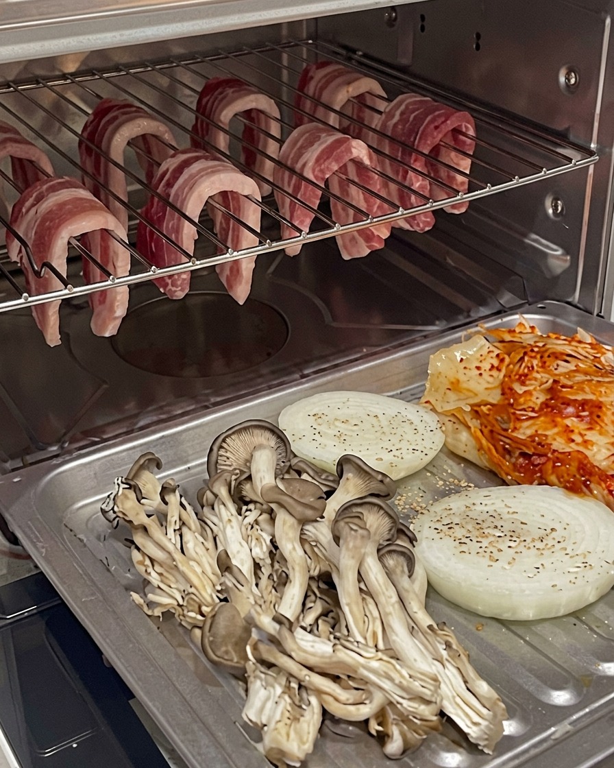 吊るされた豚バラ肉の下に、野菜を乗せた天板が置かれたオーブン内部。