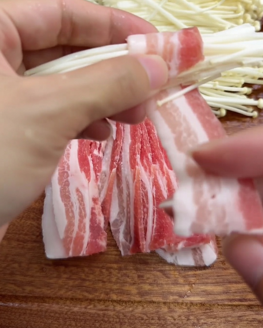 豚バラ肉でえのきの束を巻いている手元のクローズアップ。