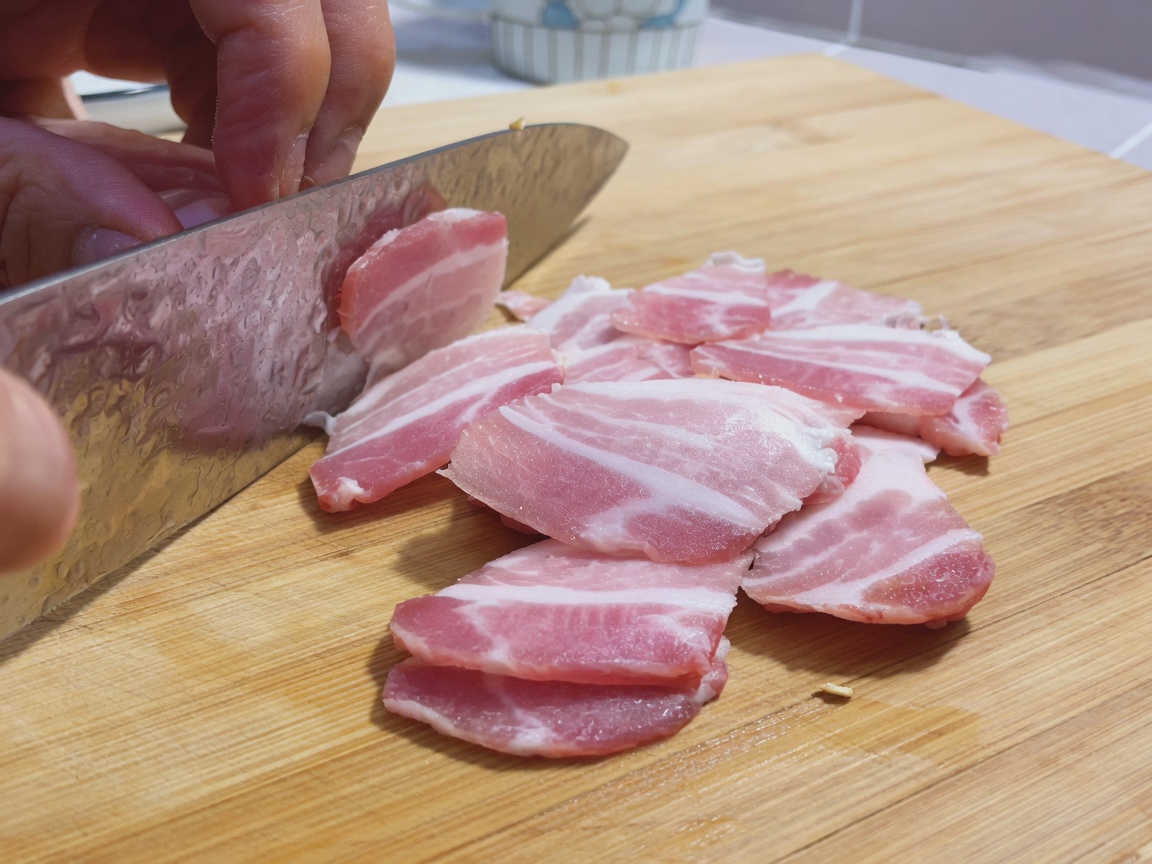 木のまな板の上で薄切りにされた生鮮の豚バラ肉と大きな包丁。