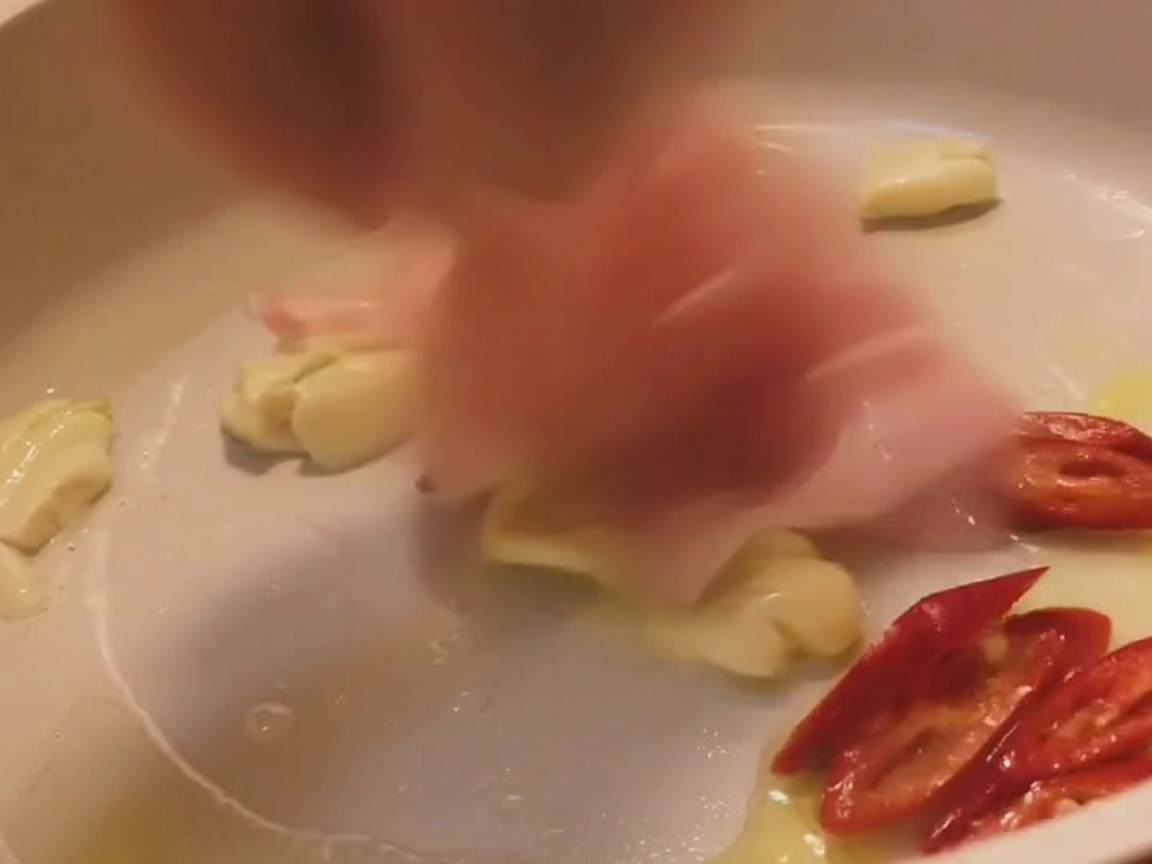 明るい色のフライパンでニンニクや赤唐辛子と一緒に炒められる豚バラ肉。