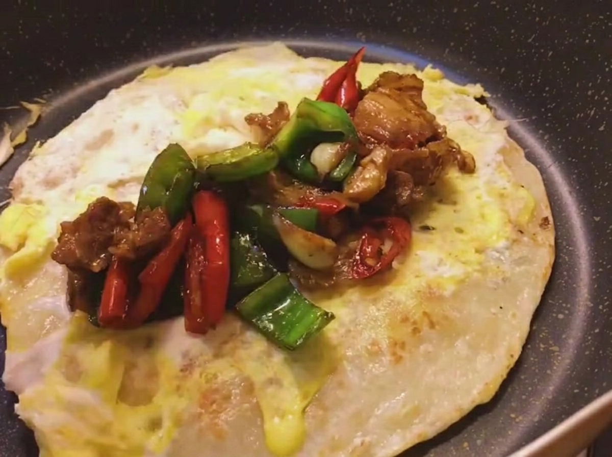 卵を重ねてこんがり焼いたネギ餅の上に、スパイシーな豚肉とピーマンの炒め物をのせている様子。