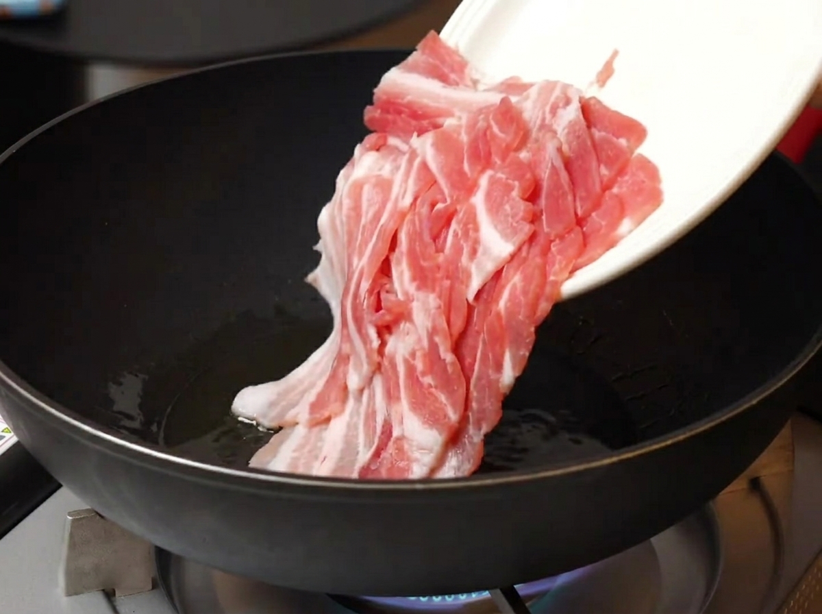 熱したフライパンに薄切りの豚バラ肉を入れる様子。