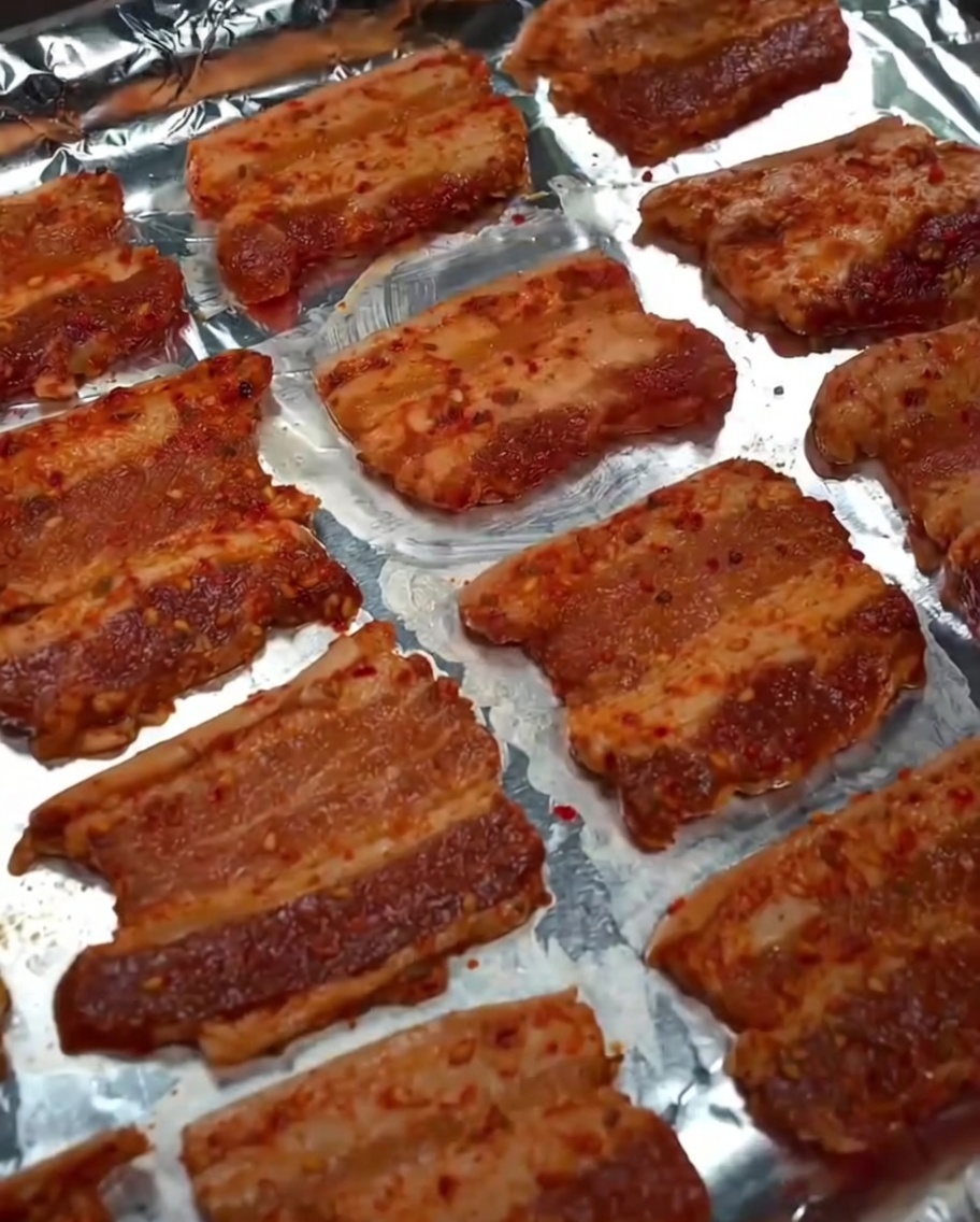天板の豚バラ肉に料理用オイルをスプレーしている様子。