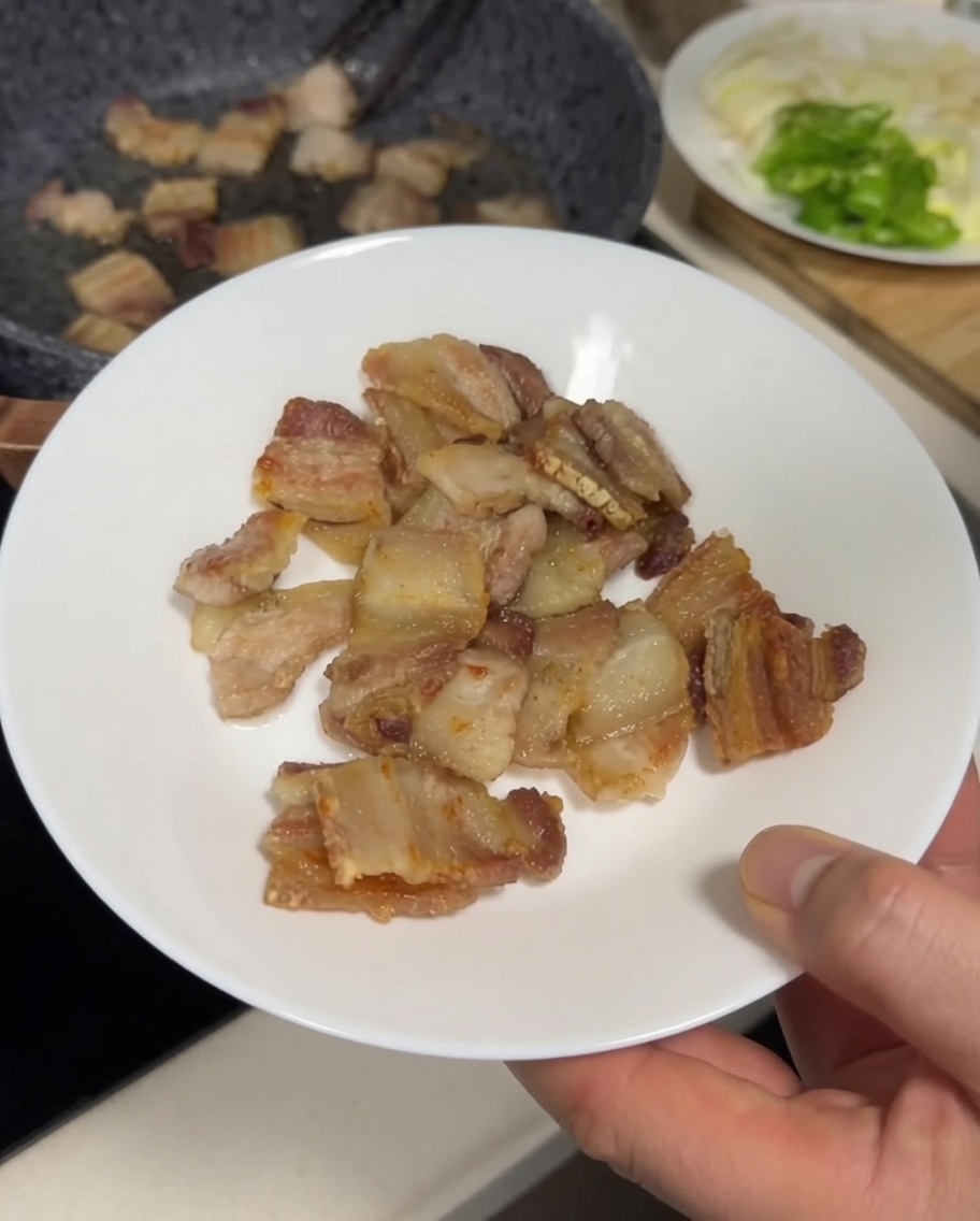 焼いた豚バラ肉をトングで皿に移している様子。