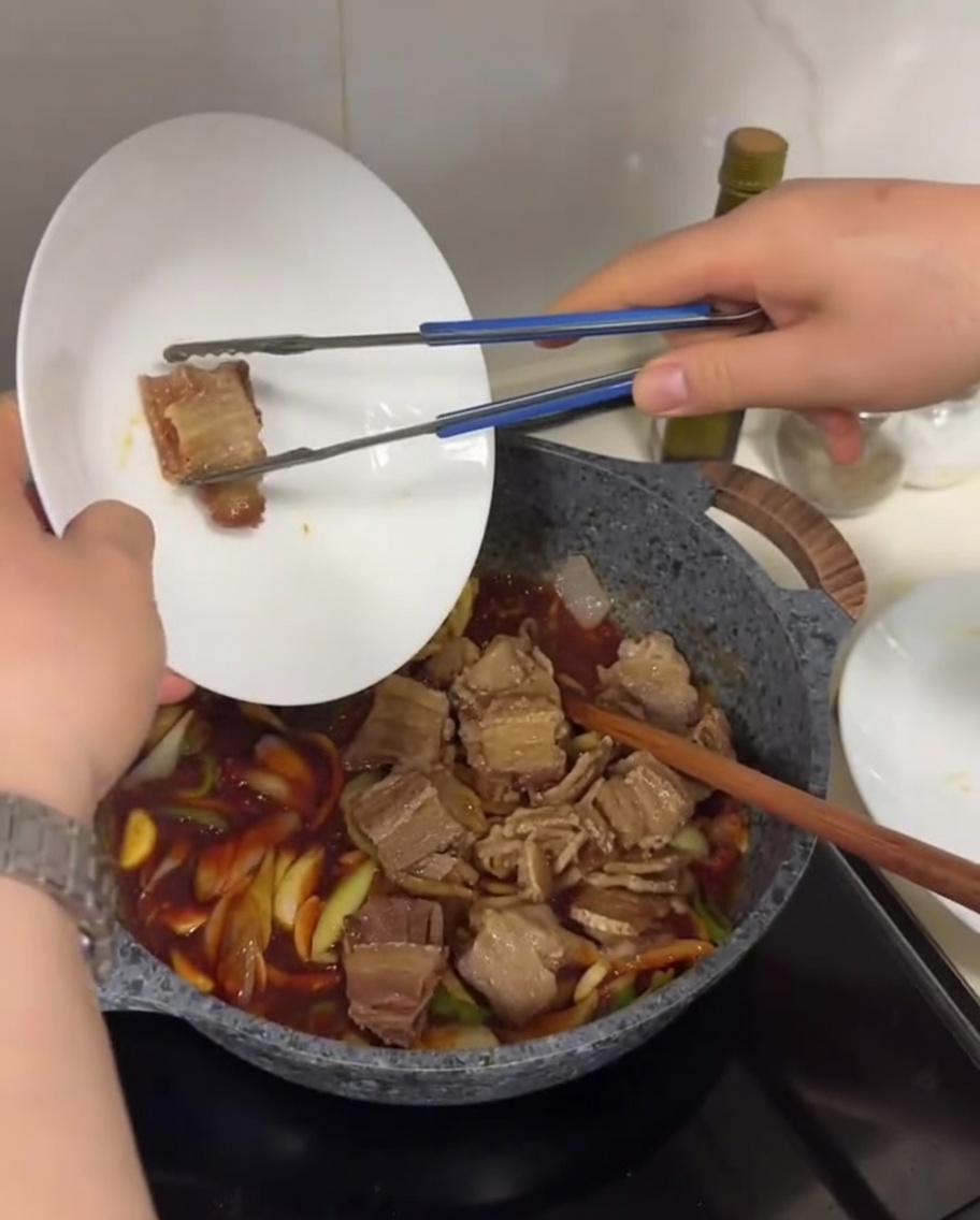 ソースと野菜が入ったフライパンに、焼いた豚バラ肉を戻し入れている様子。