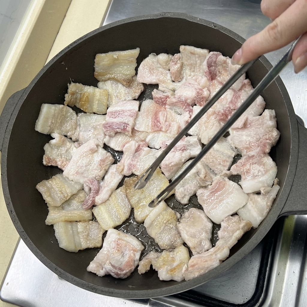 フライパンで豚バラ肉を焼き、脂が溶け出して黄金色に色づいている様子。