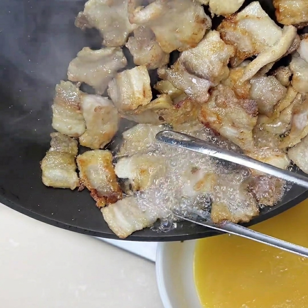 トングで肉を支えながら、フライパンから溶け出た余分な脂を器に注ぎ出している様子。