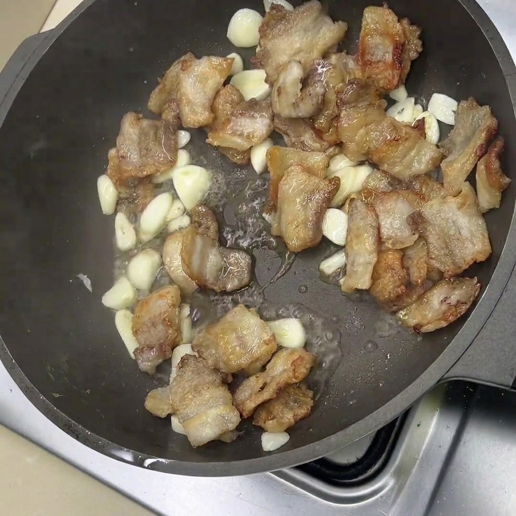 炒めた豚バラ肉とニンニクに調味料を合わせている様子。