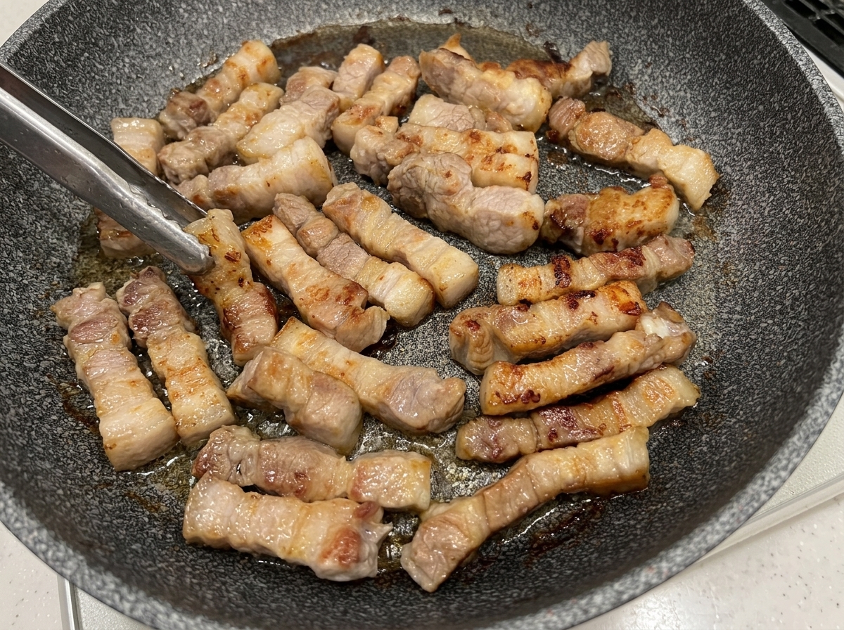 フライパンで豚バラ肉を焼き、表面がこんがりと色づいている様子。