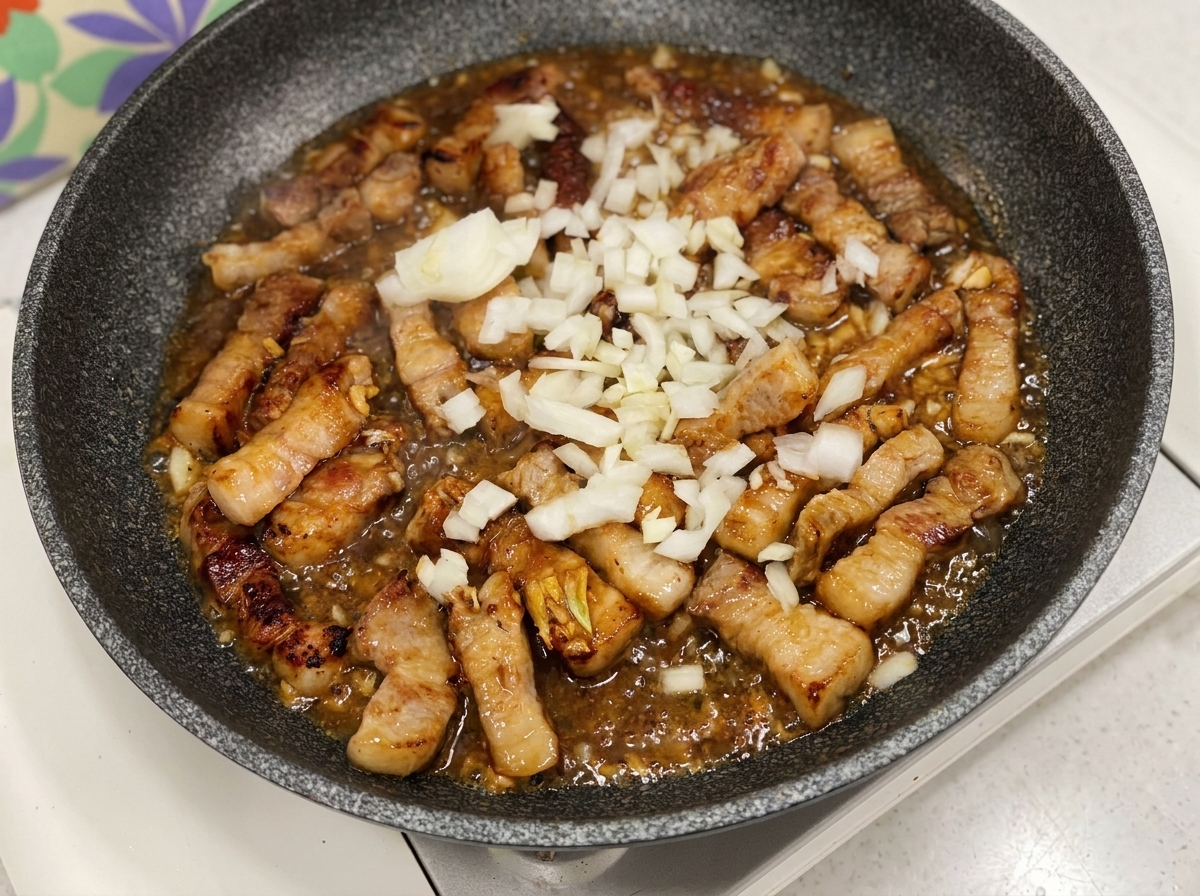 ソースが絡んだ豚肉に、角切りにした玉ねぎを加えている様子。