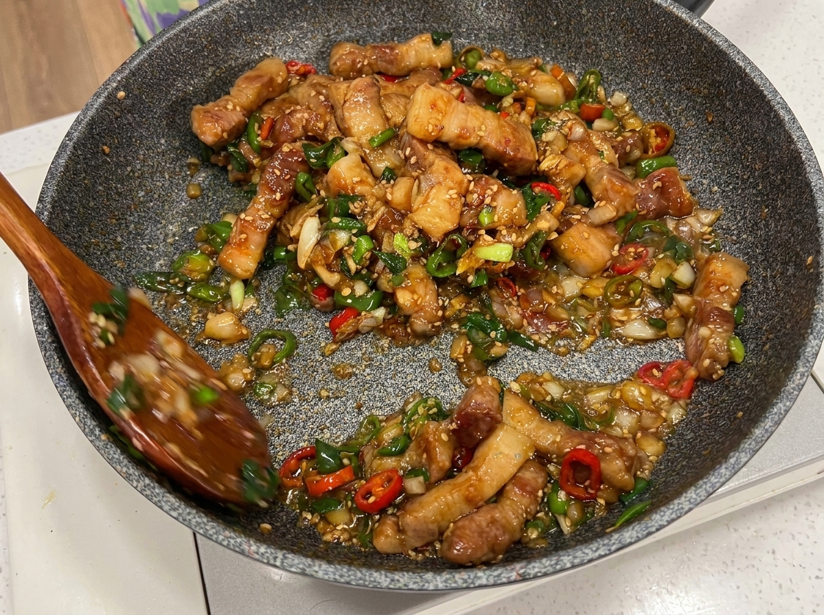 調理が完了し、ツヤのあるソースが絡んだ豚肉を木べらで混ぜている様子。