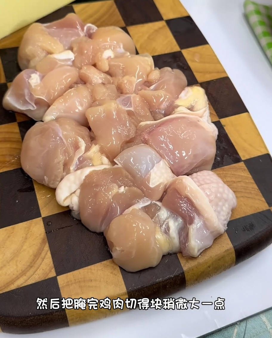 木製のまな板の上に均等な大きさに切られた生の鶏もも肉。