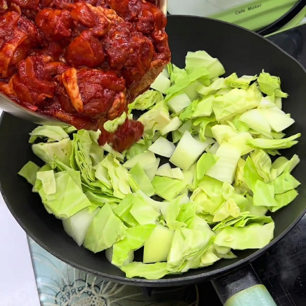 フライパンに敷いたキャベツと玉ねぎの上に、味付けした鶏肉をのせている様子。
