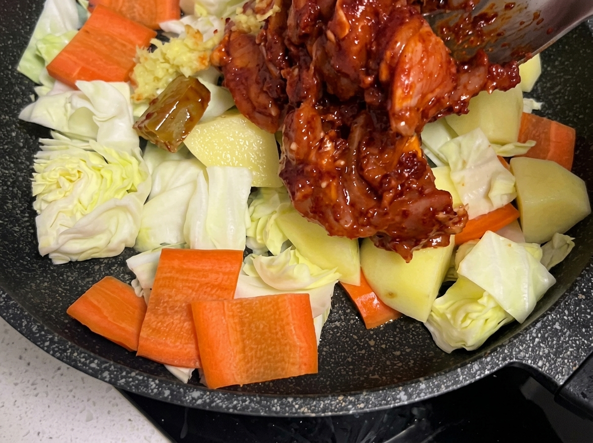 フライパンに敷いた野菜の上に、マリネした鶏肉を丁寧にのせている様子。