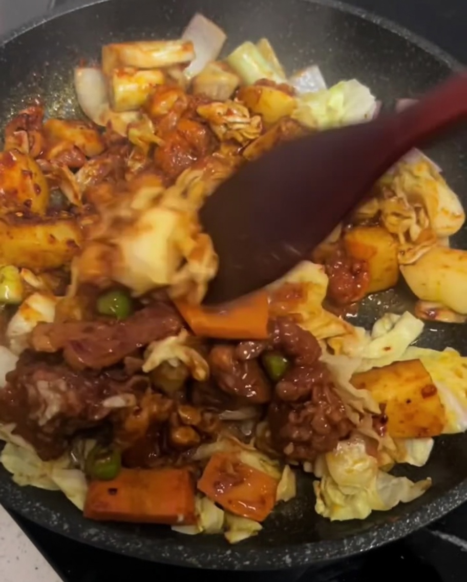 熱したフライパンの中で、スパチュラを使って鶏肉と野菜を優しく混ぜ合わせている様子。