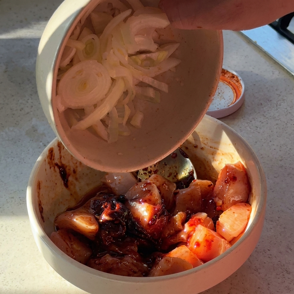 調味料を和えた鶏肉にスライスした玉ねぎとにんにくを加えている様子