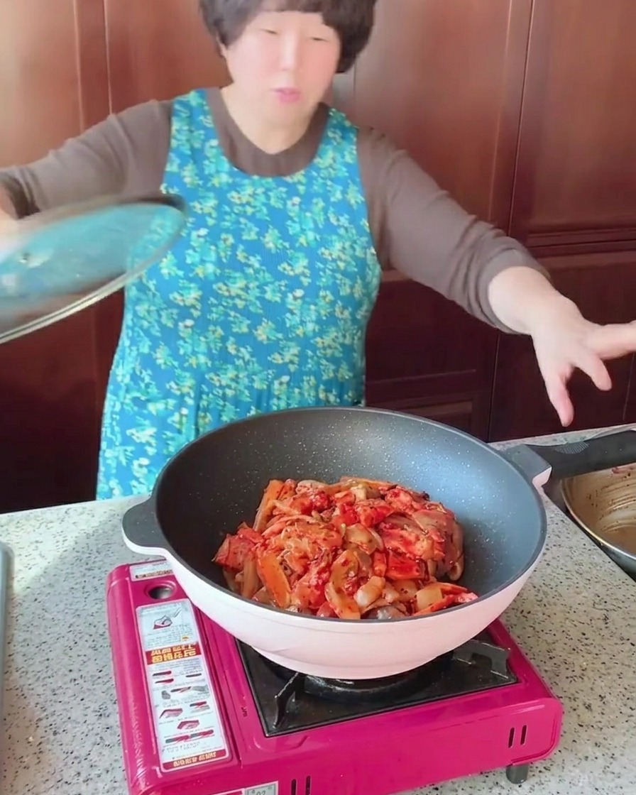豚バラ肉とイカ、野菜が炒められており、透明なガラスの蓋で覆われているフライパン。