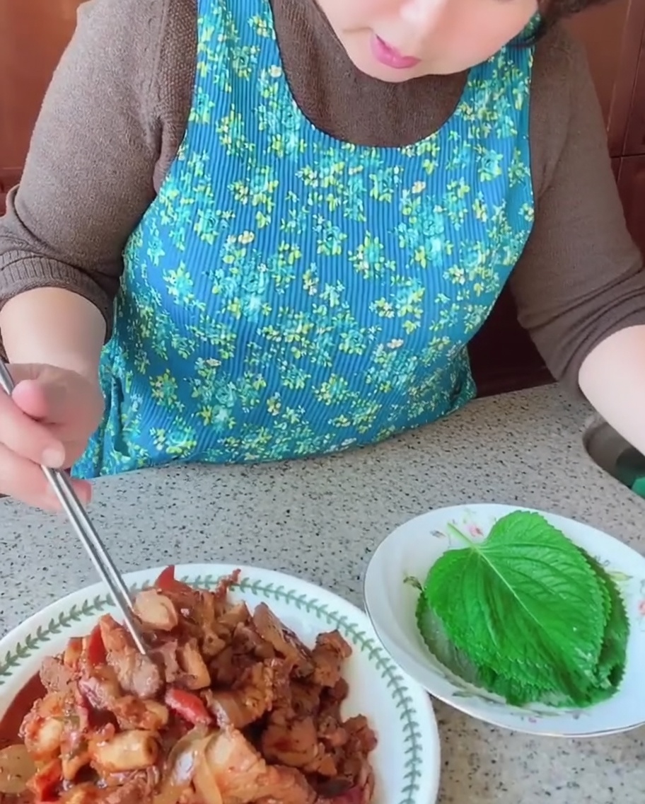 箸を使って、調理した豚バラ肉とイカを新鮮なエゴマの葉に乗せている様子。
