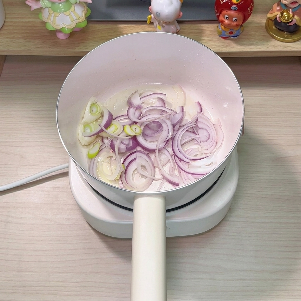 鍋で玉ねぎと長ねぎをツナの油で炒めている様子。