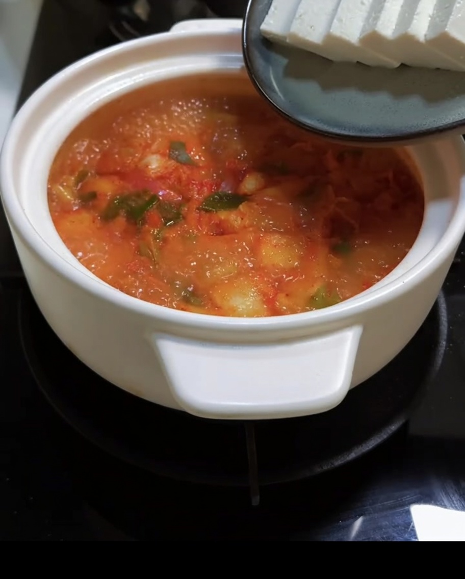 沸騰した赤いスープにスライスした豆腐を加えている様子。