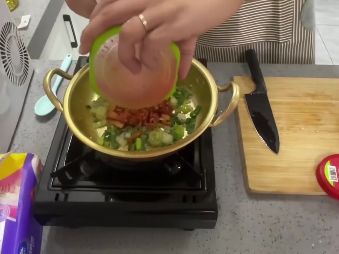 炒めた香味野菜の上に刻んだキムチを入れている様子。