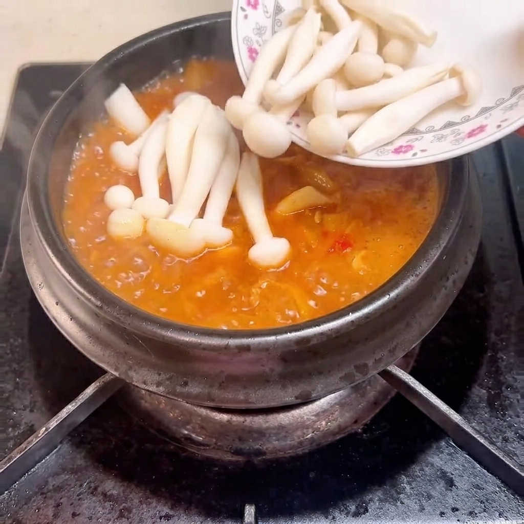 ぐつぐつ煮え立つ土鍋のスープにきのこを入れている様子。