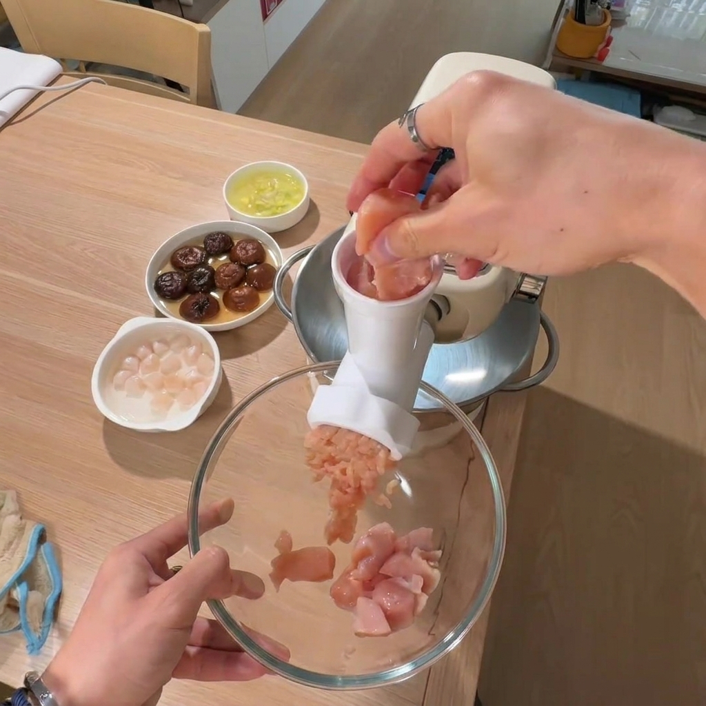 大きなボウルに鶏ひき肉を入れ、背景に椎茸と貝柱が入ったボウルが置かれている様子。