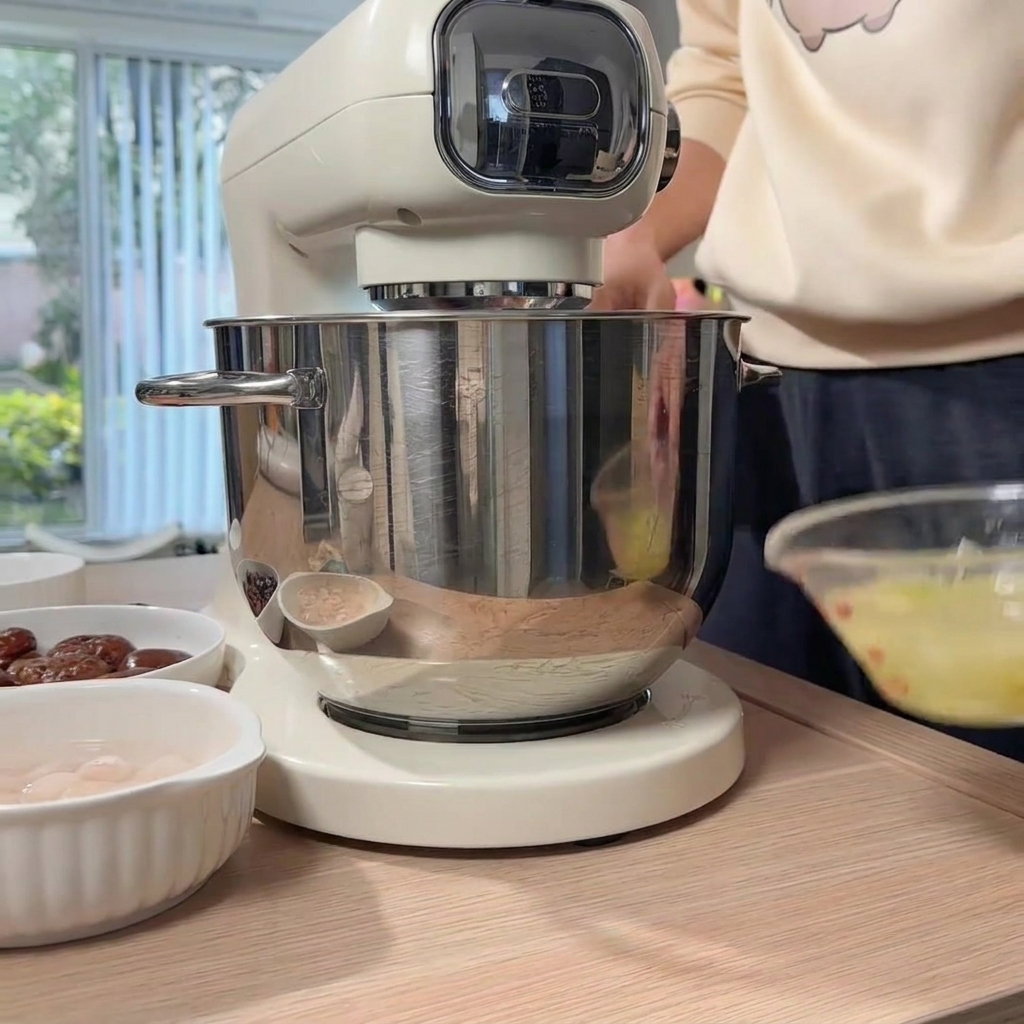 スタンドミキサーのボウルに入った鶏肉に、準備した生姜ねぎ水を注ぎ入れている手。