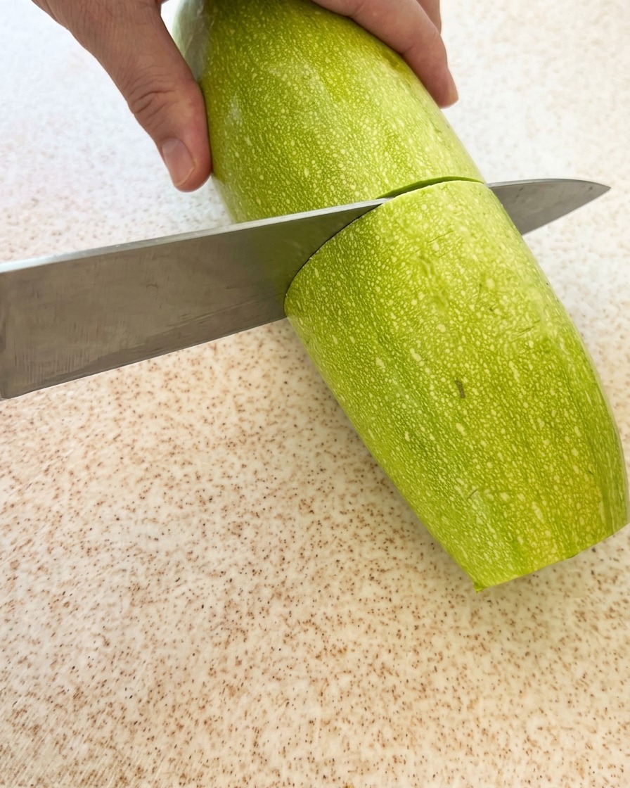 まな板の上で緑色のズッキーニを輪切りまたは半月切りにしている様子。