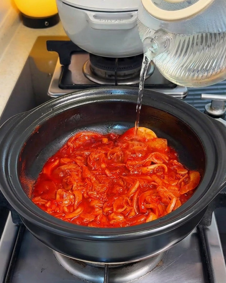 炒めたキムチのベースが入った鍋に水を注いでいる様子。