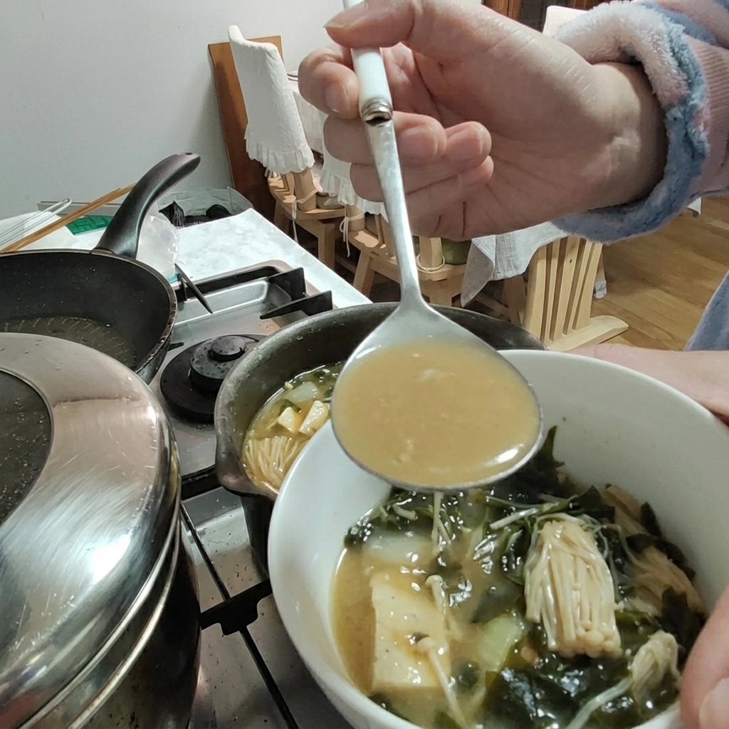 お玉で味噌をスープに溶かしている様子。豆腐とえのきが見える。