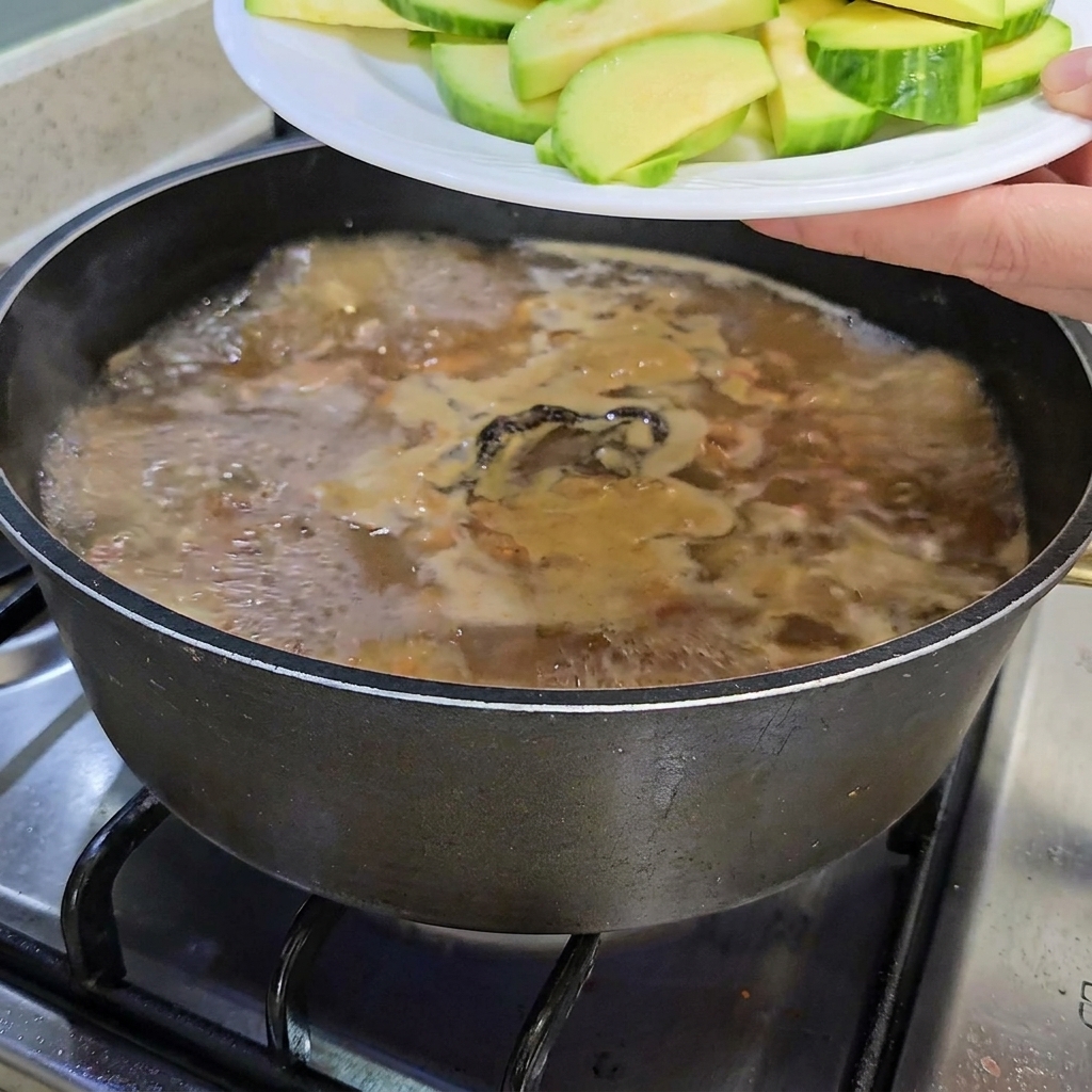 スライスしたズッキーニとえのき茸を煮え立つチゲ鍋に加えている様子。