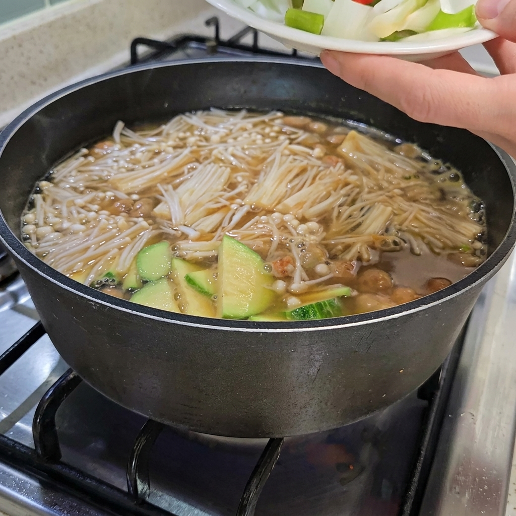 刻んだ玉ねぎ、ねぎ、赤と青の唐辛子を、スライスした豆腐が入ったチゲに加えている様子。