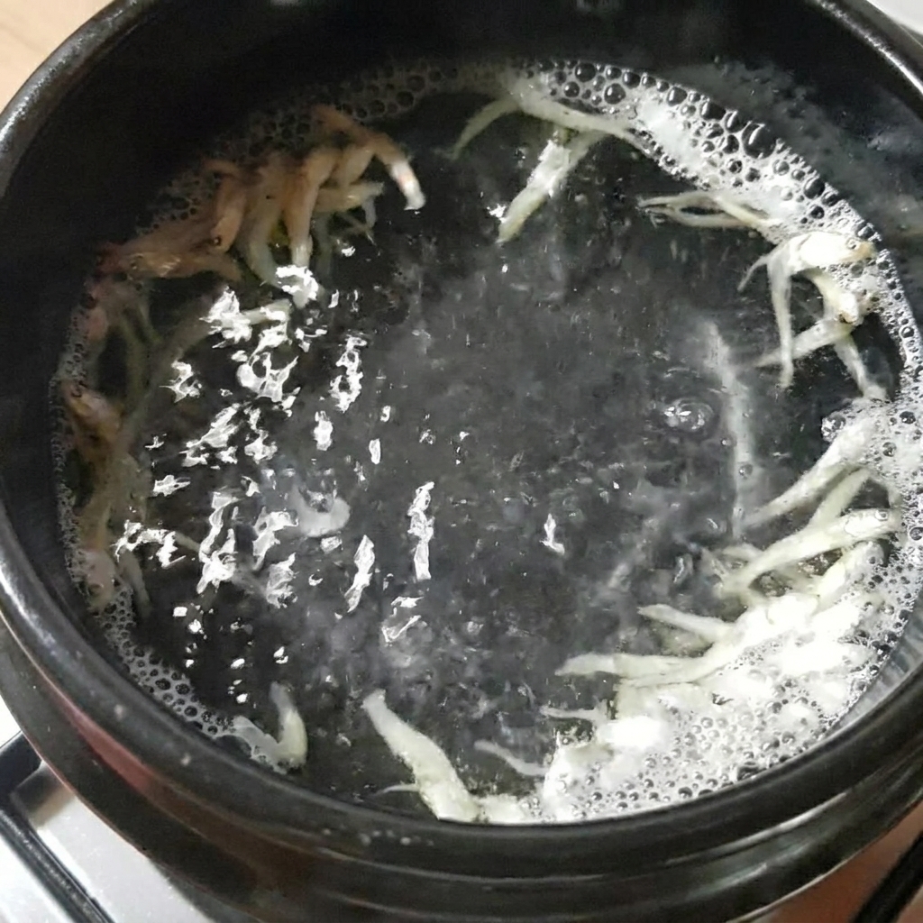 黒い石鍋に水、煮干し、昆布を入れ、コンロで沸騰させている様子。