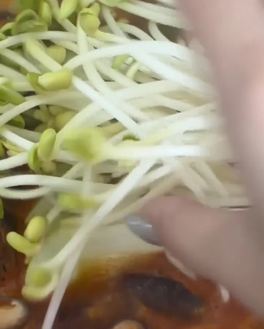 鍋に豆もやしをひとつかみ加える様子。