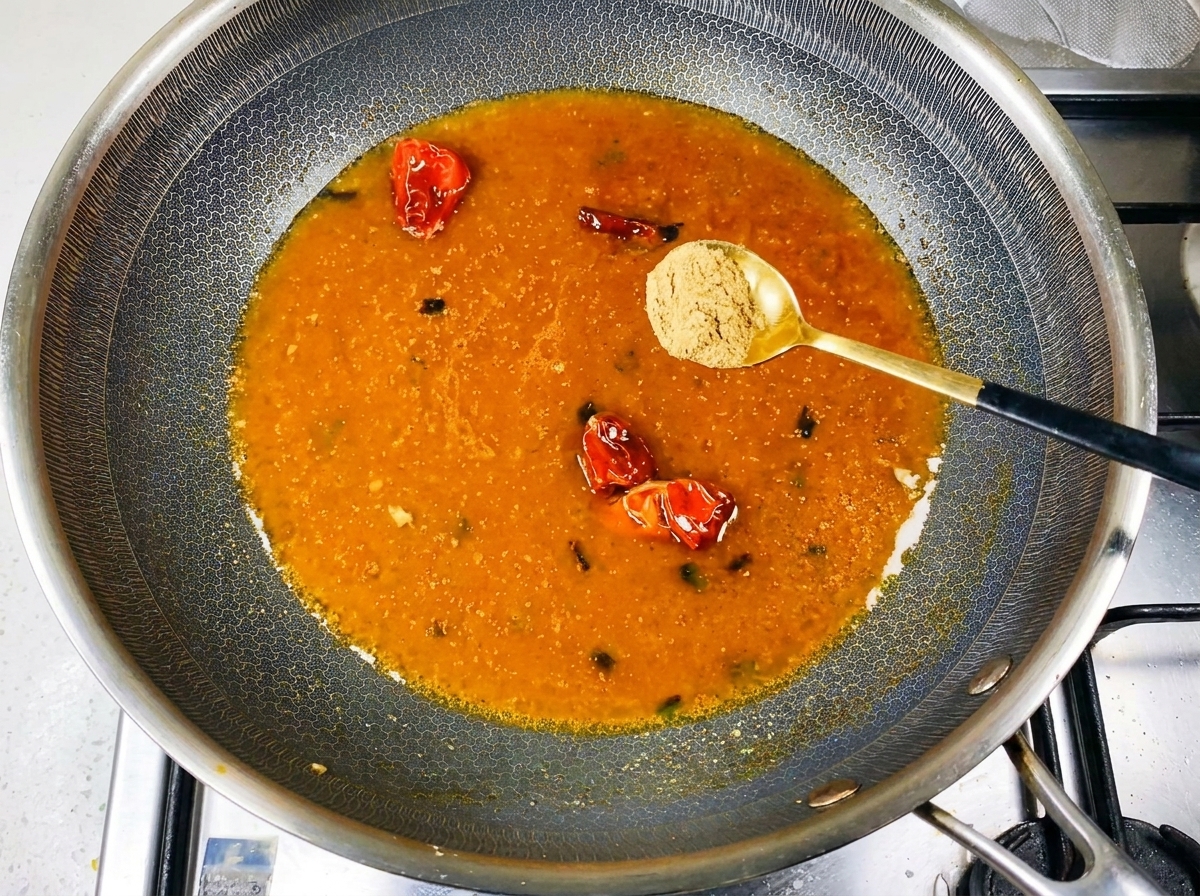 中華鍋で煮立っているオレンジ色のスープにスパイスパウダーを振りかけている様子。