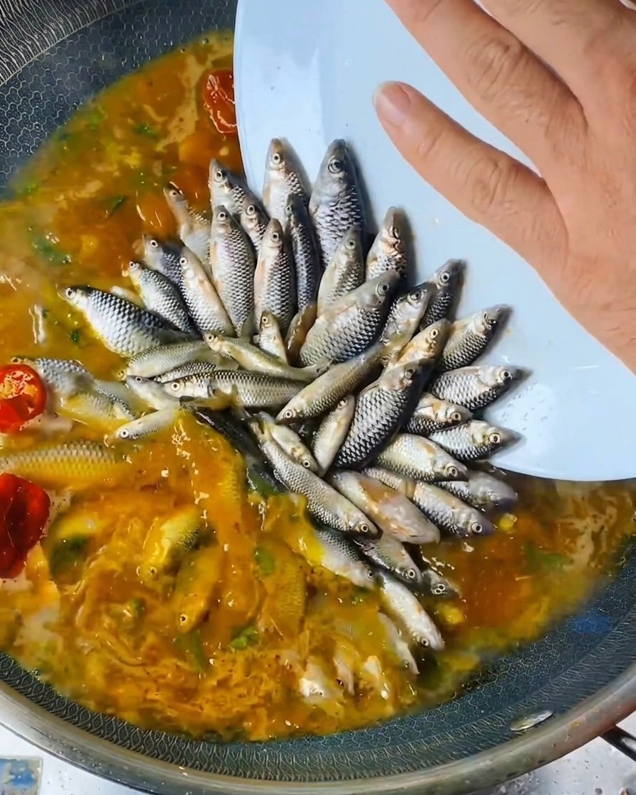 鍋に並べた魚の上からボトルに入った液体調味料を注いでいる様子。