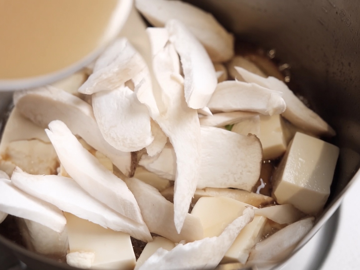 豆腐とエリンギが入った鍋に、溶いた味噌を注ぎ入れている様子。