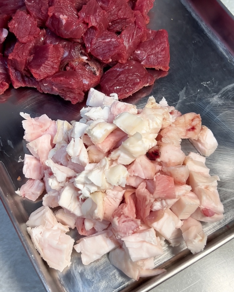 ステンレスボウルに入った牛ひき肉に塩と黒こしょうで下味をつけている様子。