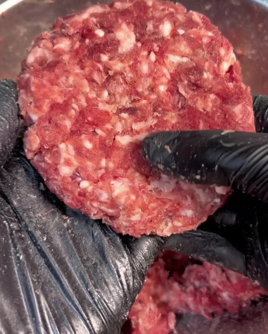 黒い手袋をした手で、味付けしたひき肉を丸く形作っている様子。