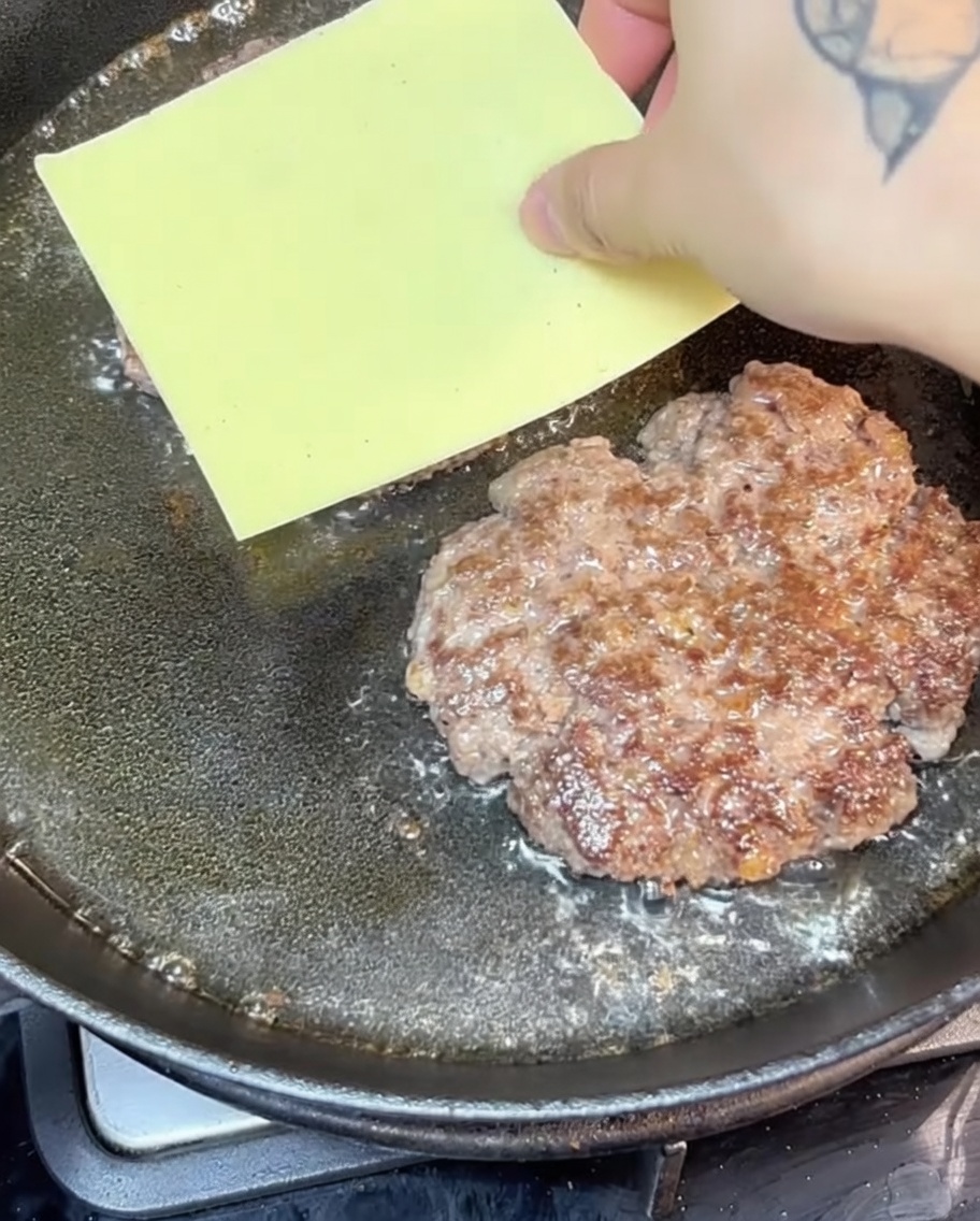 フライパンの中でチーズがパティの上に溶けている様子。