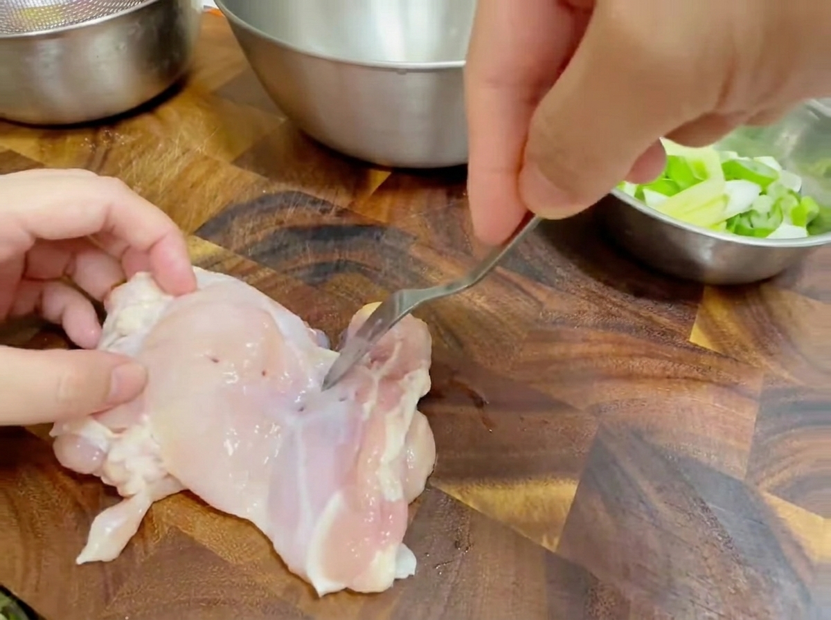 まな板の上で鶏もも肉にフォークを刺している様子