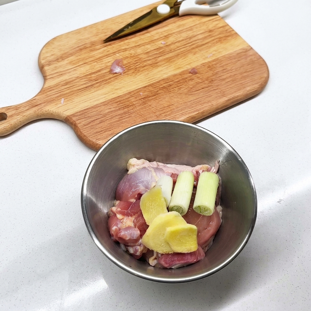 金属製のボウルに、鶏肉、スライスしたしょうが、長ねぎが入っている様子。