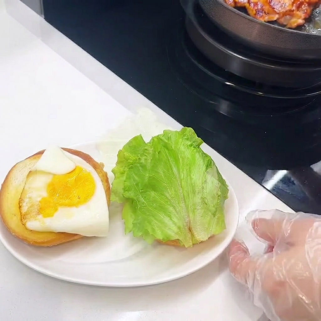 トーストしたバンズにチキン、チーズ、目玉焼き、レタスを重ねている様子。