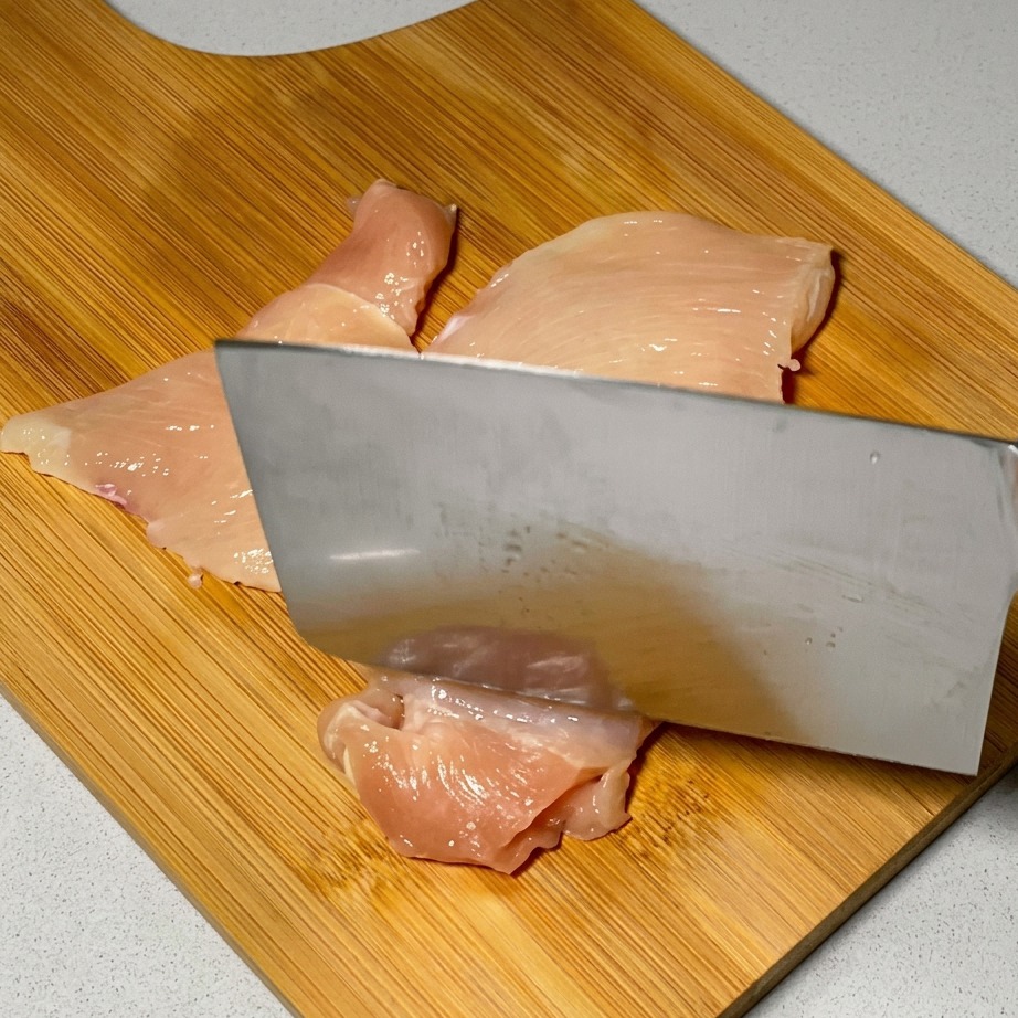 大きな包丁の背を使って鶏肉を叩いている様子。