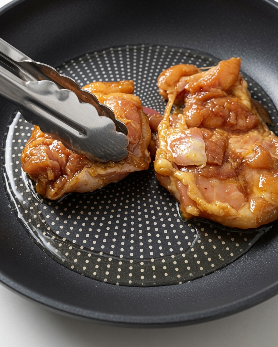 熱したフライパンに、タレに漬けた生鶏肉をトングで広げている様子。