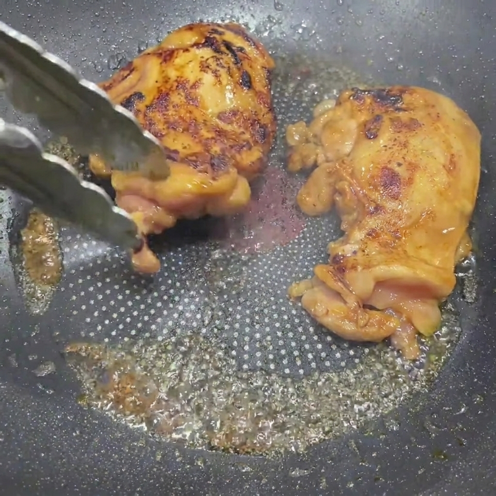 テリヤキソースが絡み、きつね色に焼けた鶏肉をトングで裏返している様子。