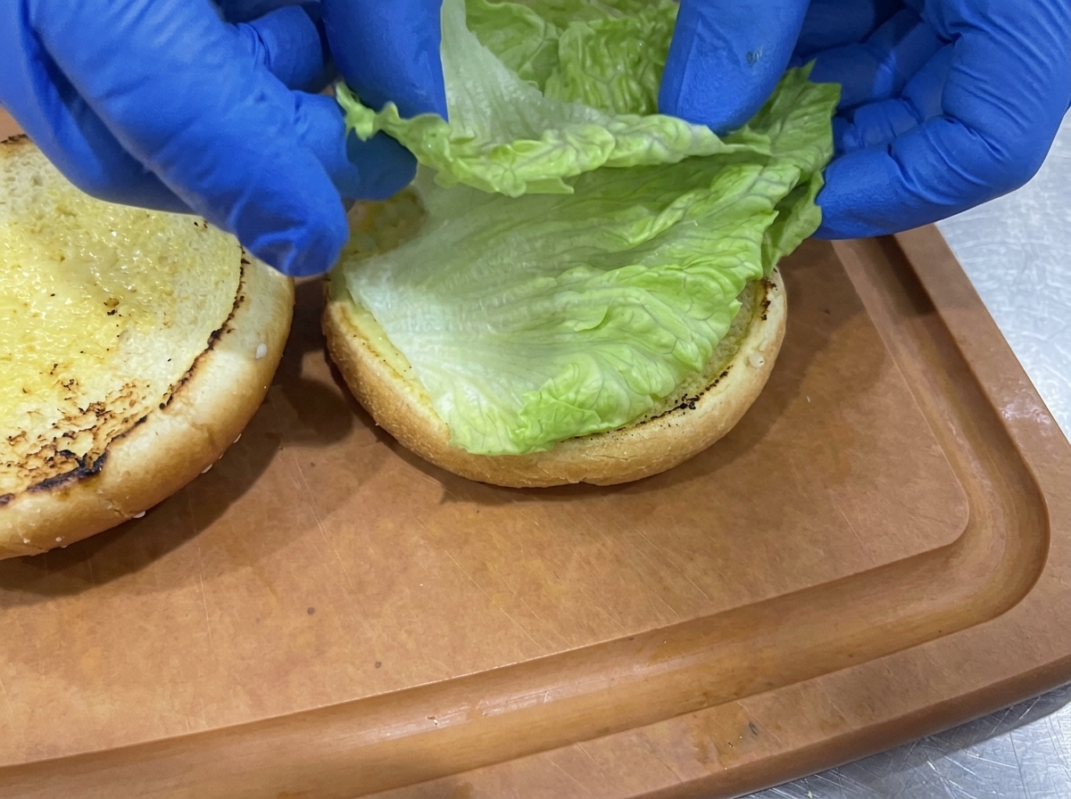 焼いたバンズの下半分に、レタスを重ねている様子。