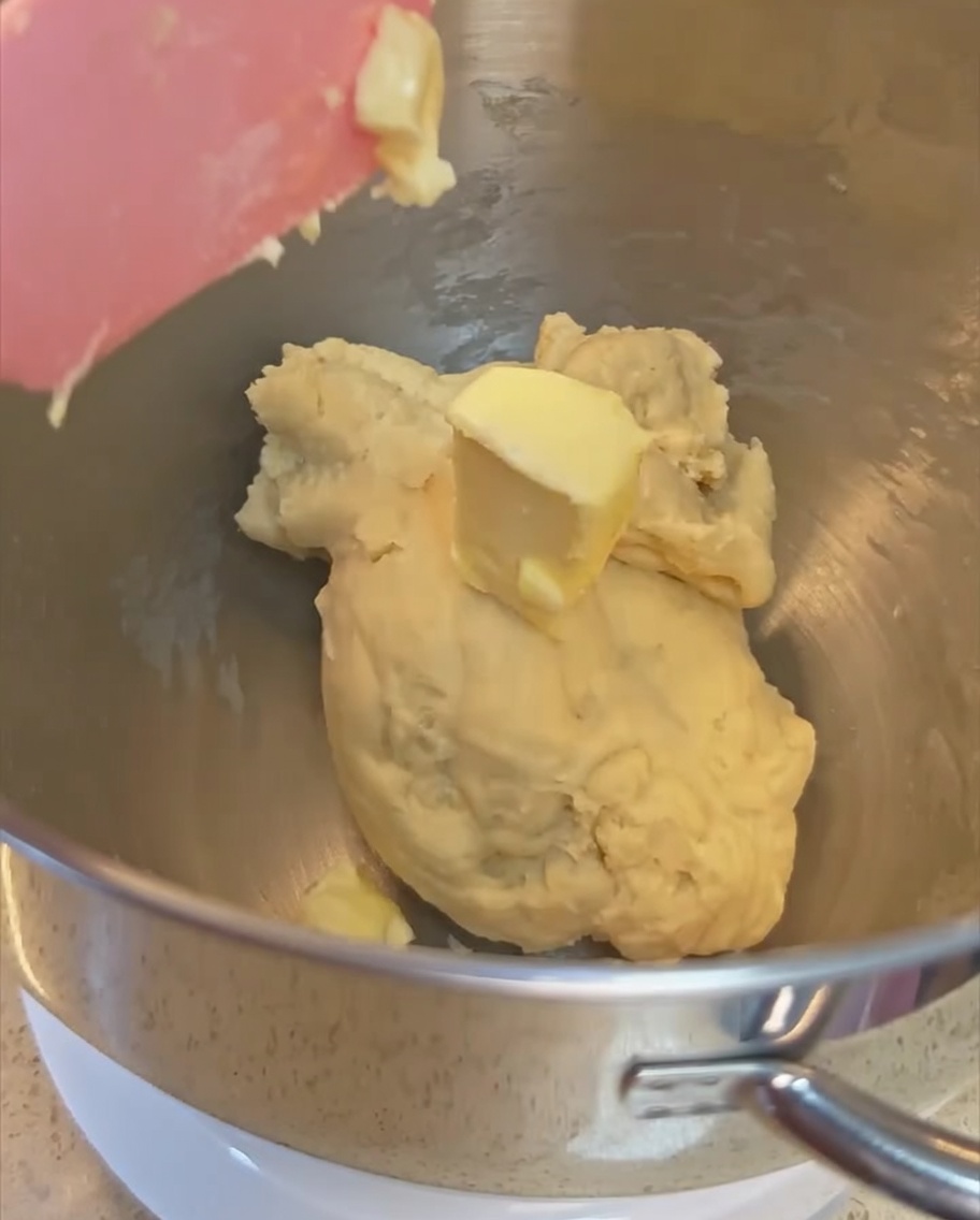 ステンレス製のボウルの中でまとまり始めた生地にバターを加えている様子。